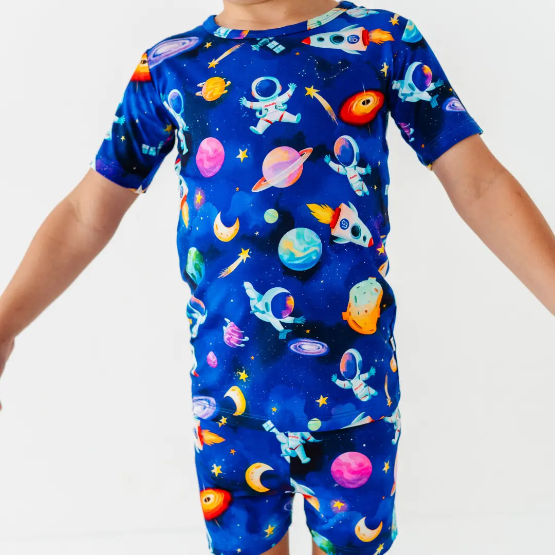 Close-up of a child in a blue space print short pajama set with astronauts, planets, and shooting stars.